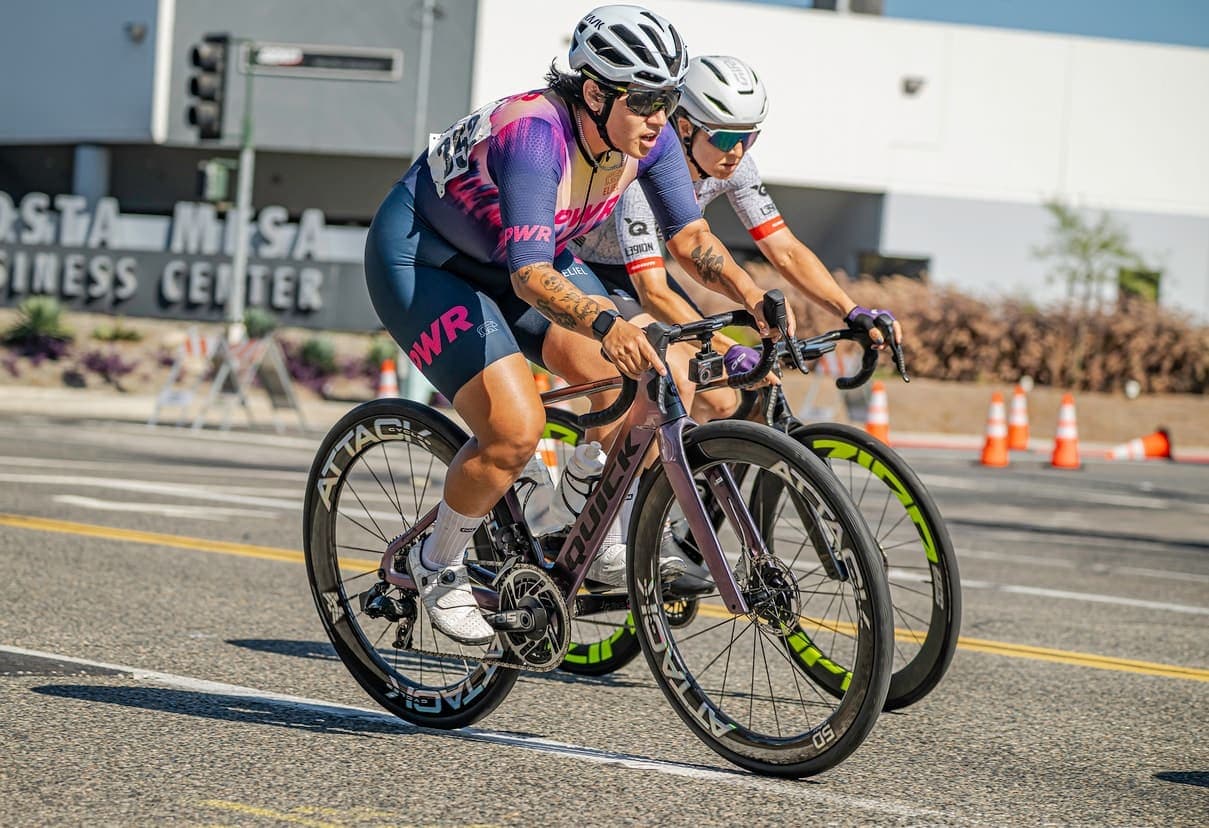 Two riders on ATTACKCYCLES wheels cornering through a criterium.